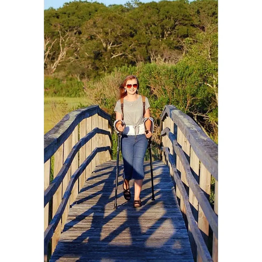 Young woman with forearm crutches on a walking path bridge